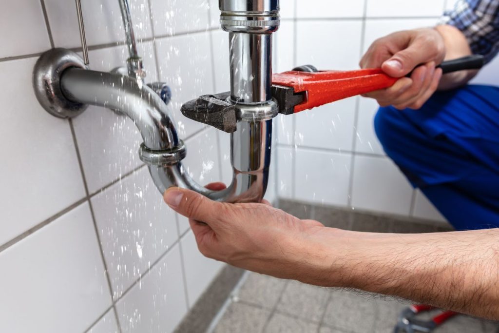 photo of a plumber tightening a wrench around the gasket of leaky plumbing